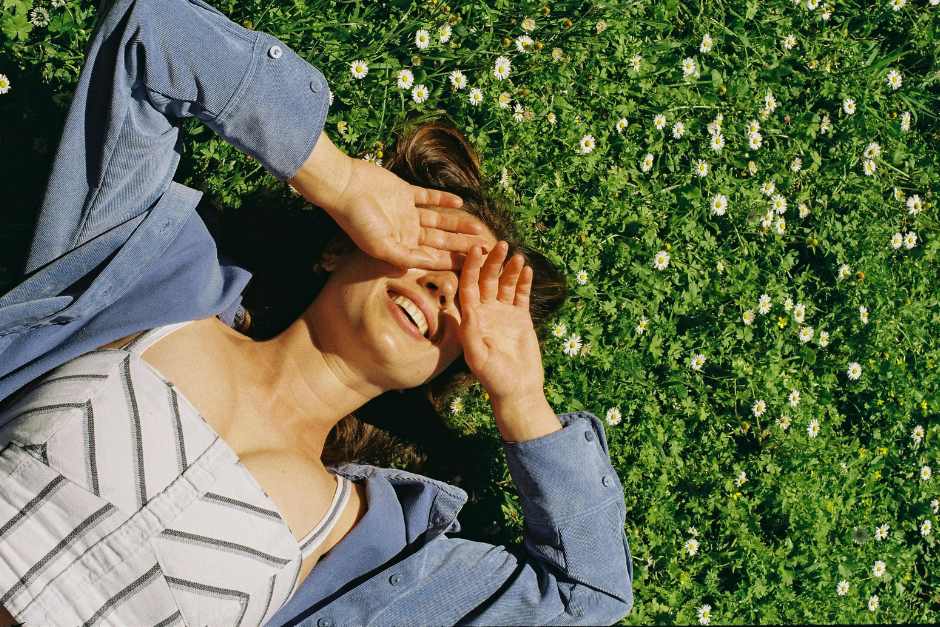 Woman with her hands covering her eyes, lying in a field of daisies_Learn How to Forgive Yourself Blog Post