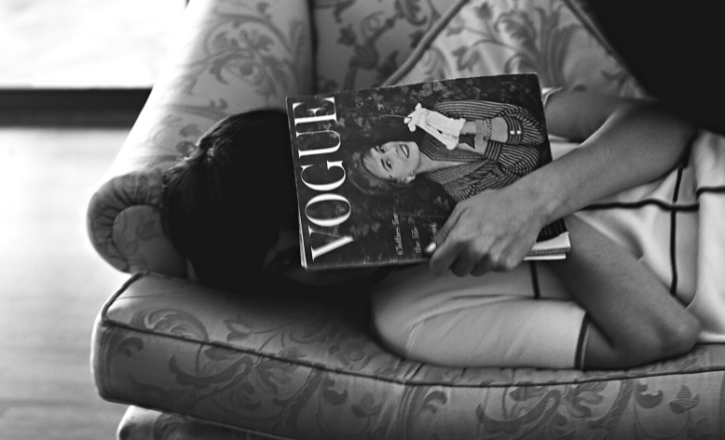 Emotionally unavailable woman hiding face with Vogue magazine lying on a sofa.