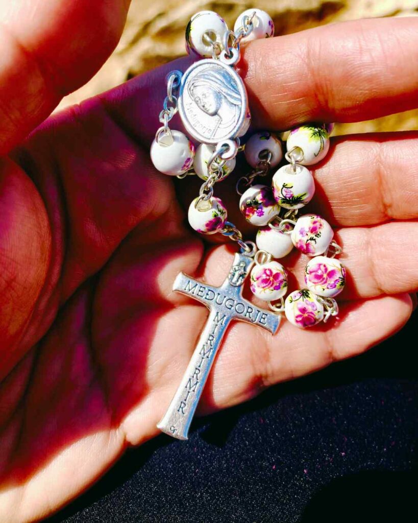 A pink and white Medjugorje rosary in the palm of a hand