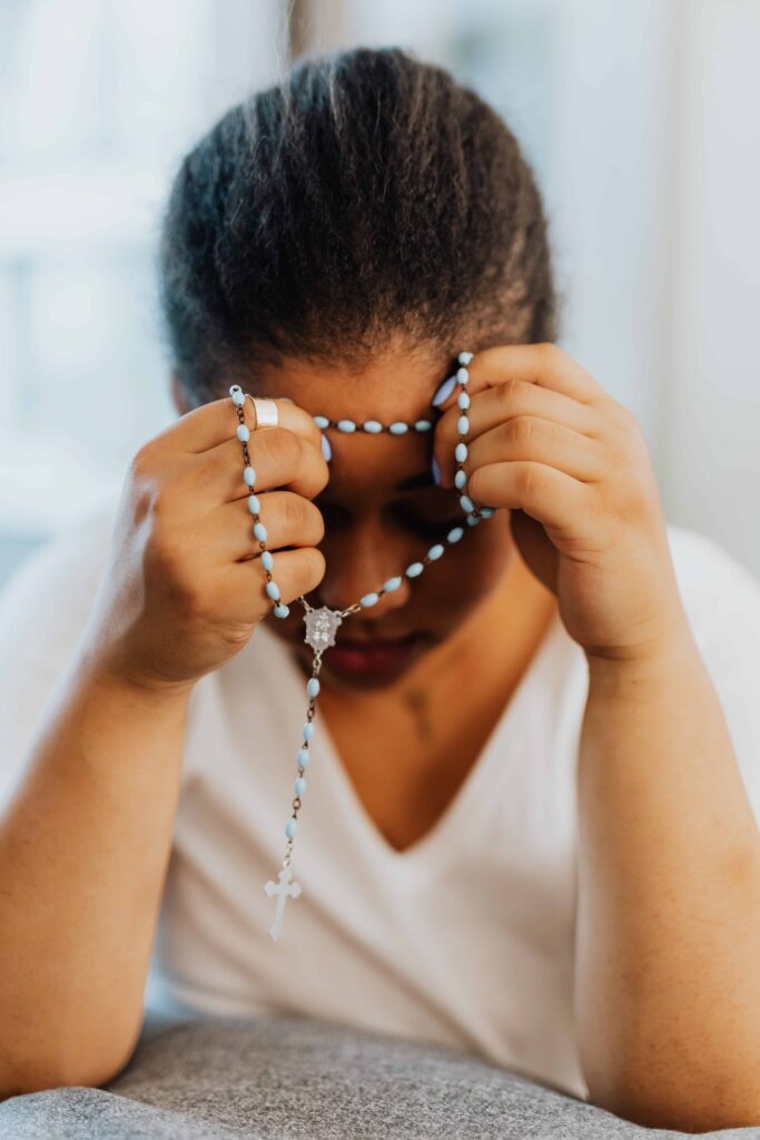 Woman kneeling in a spiritual coaching session holding a rosary.